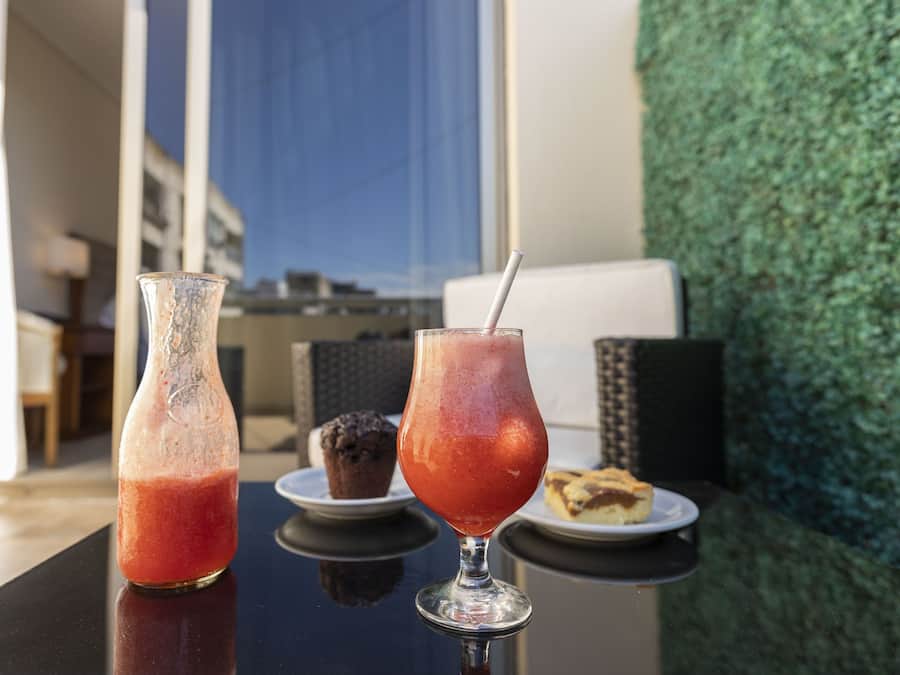 Una mesa con un vaso de bebida roja, un vaso de bebida helada y un muffin en un plato.