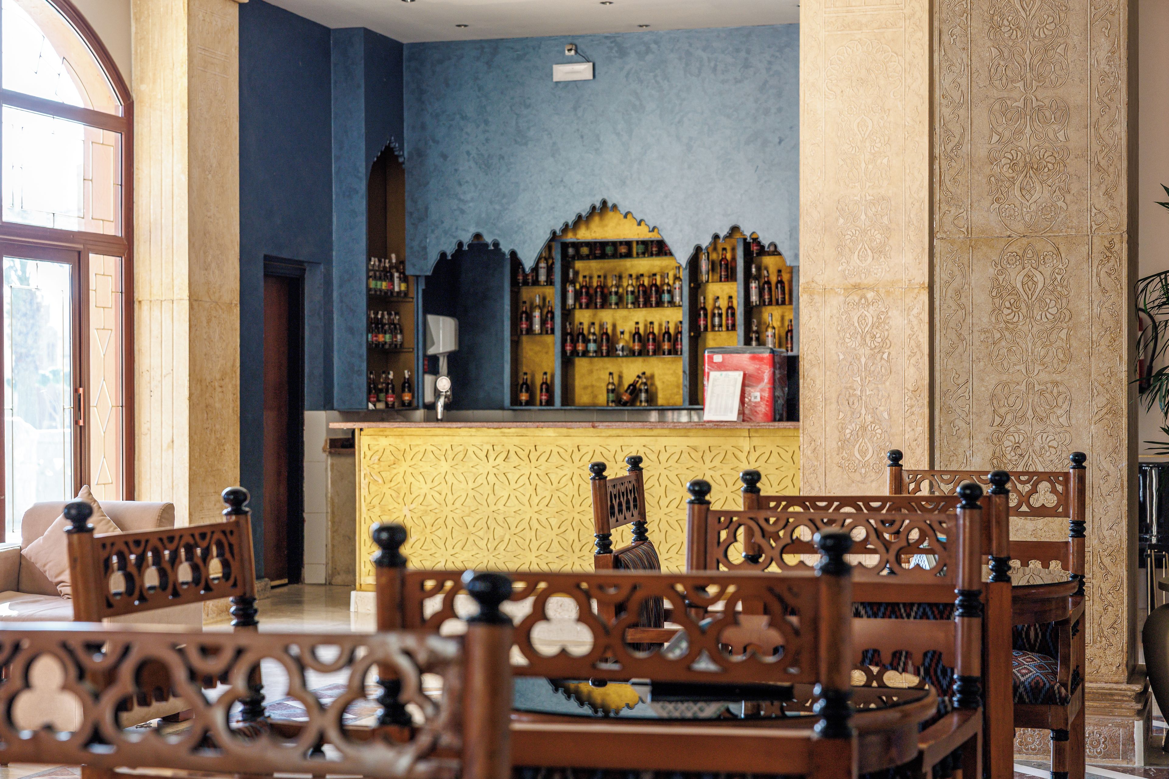 A bar area with a blue wall, wooden chairs, and a counter with bottles.