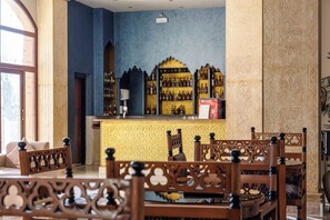 Un espace bar avec un mur bleu, des chaises en bois et un comptoir où sont exposées des bouteilles.
