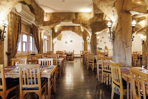 A restaurant with wooden tables and chairs, stone walls, and hanging light fixtures.