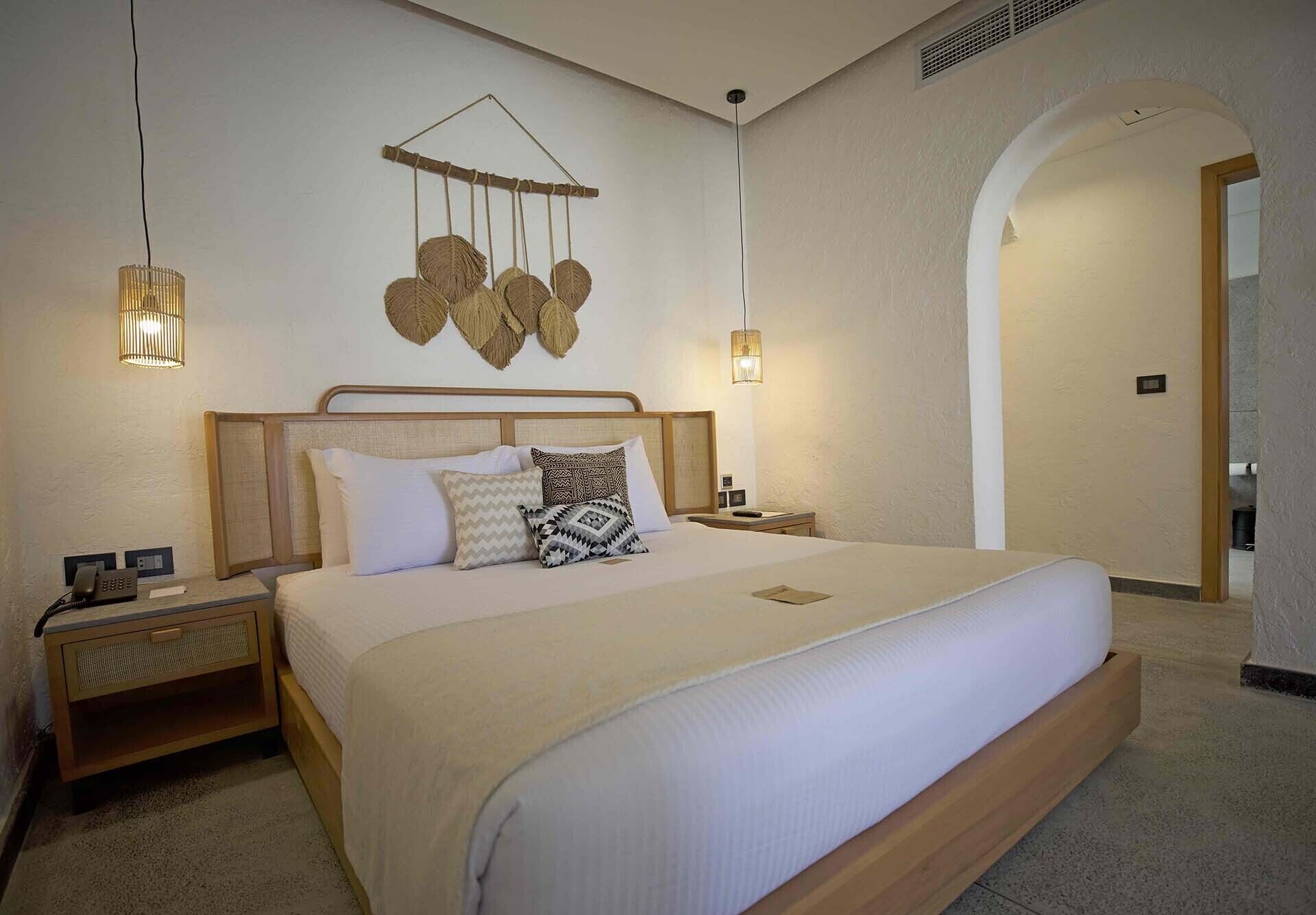 Ein Hotelzimmer mit einem großen Bett, zwei Nachttischen, einer Wandleuchte und einem Rundbogenportal.