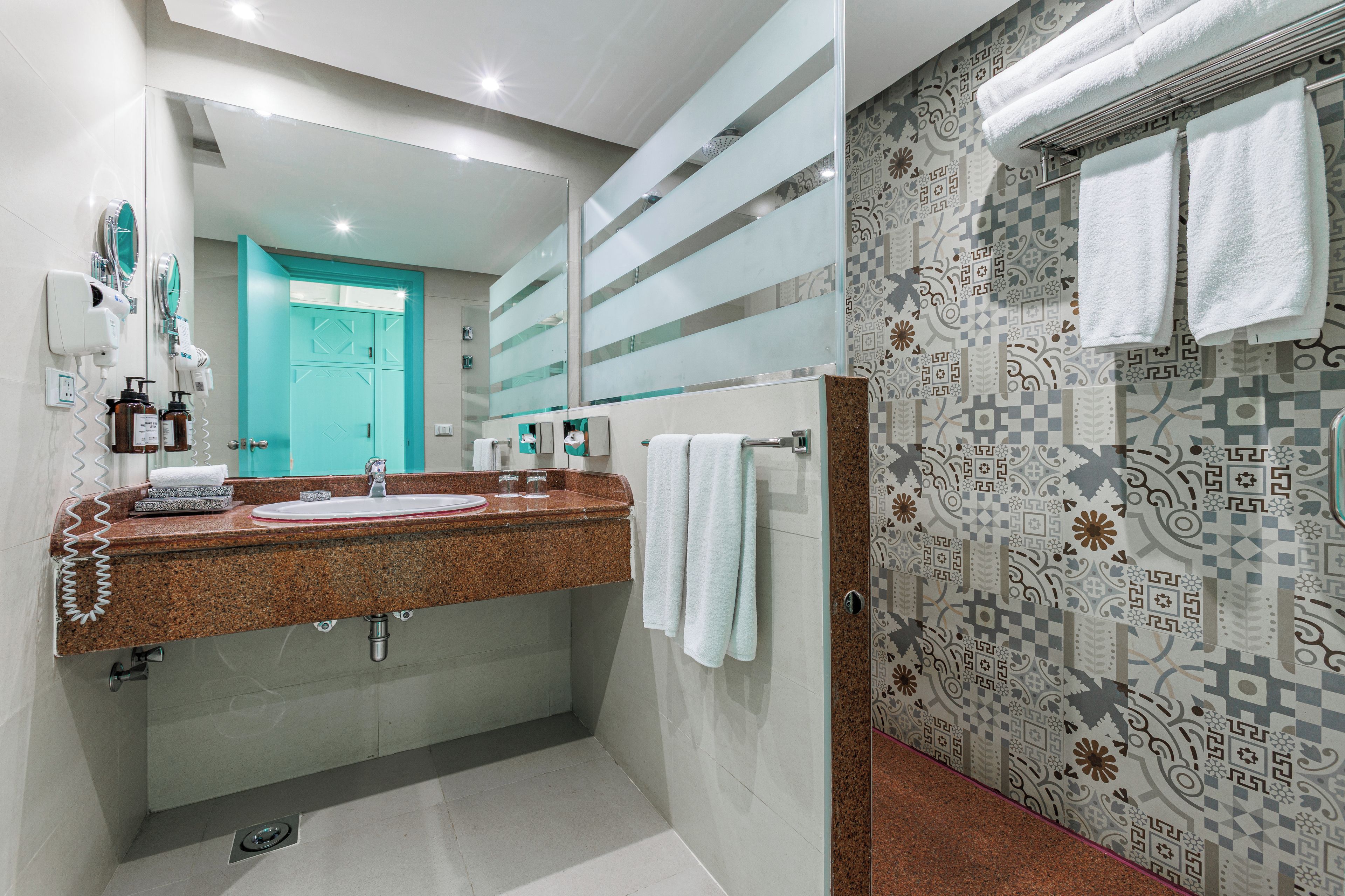 A bathroom with a granite countertop sink, a mirror, a towel rack, and patterned wall tiles.