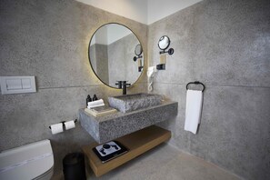 Un bagno moderno con lavabo in granito, uno specchio grande, uno specchio da mano, un portasciugamani, un water e un piccolo ripiano con bilancia digitale.