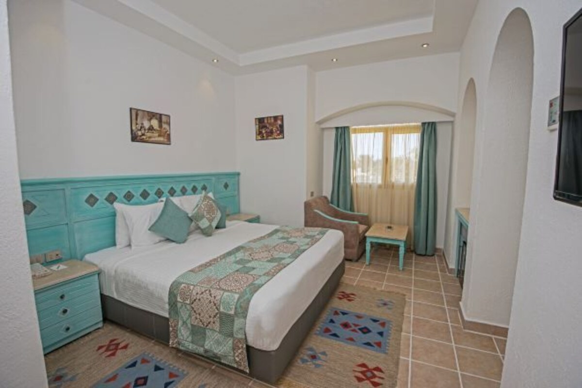 A hotel room with a bed, a chair, a desk, and a window with curtains.