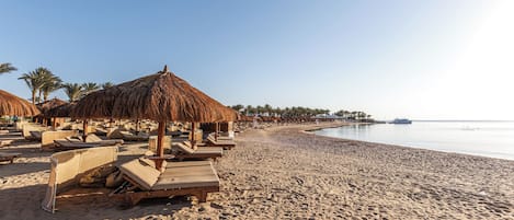 A beach with sun loungers and thatched umbrellas, a sandy shore, and a calm sea.