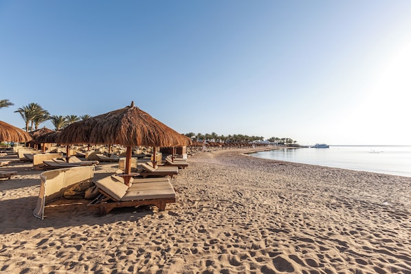 A beach with sun loungers and thatched umbrellas, a sandy shore, and a calm sea.