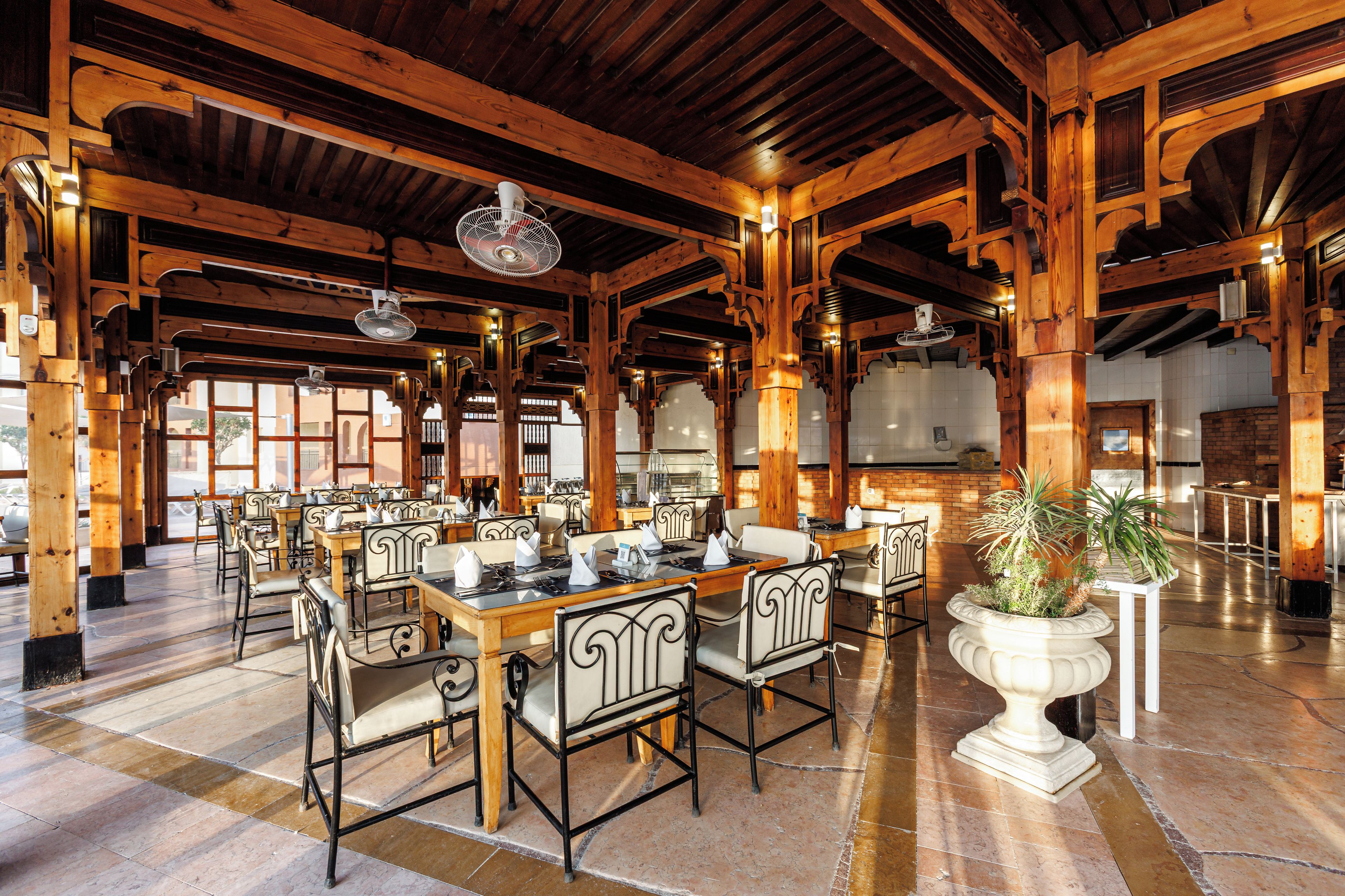 Un comedor interior espacioso con vigas de madera, mesas dispuestas para comer y una planta grande en maceta.