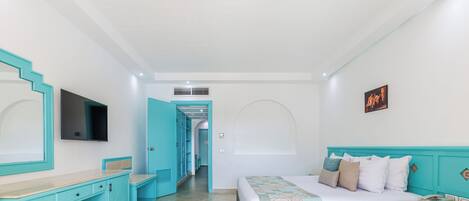 Habitación de hotel con cama, escritorio, silla, televisor y baño visible a través de una puerta abierta.