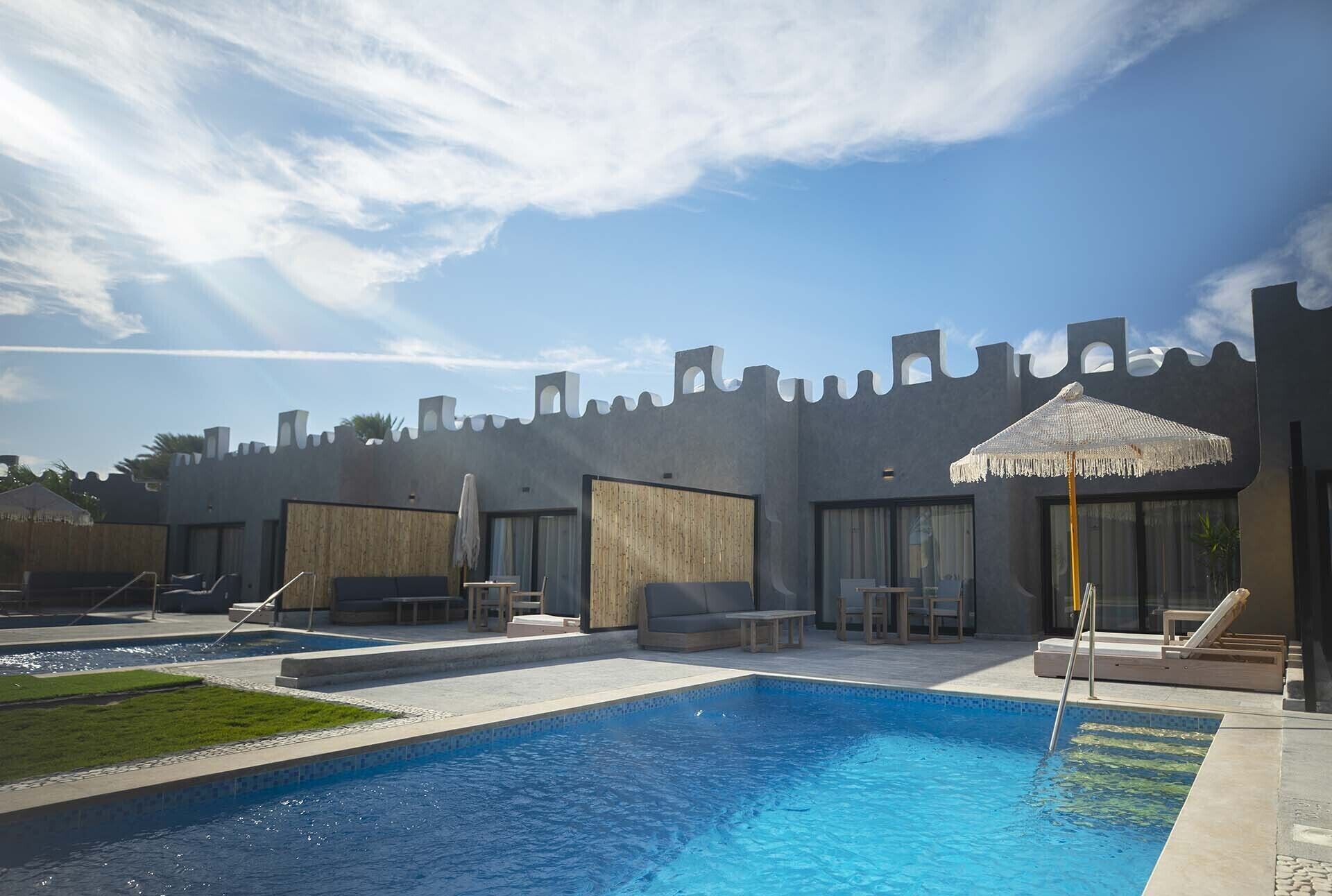 A pool area with a castle-like wall, lounge chairs, and a small table.
