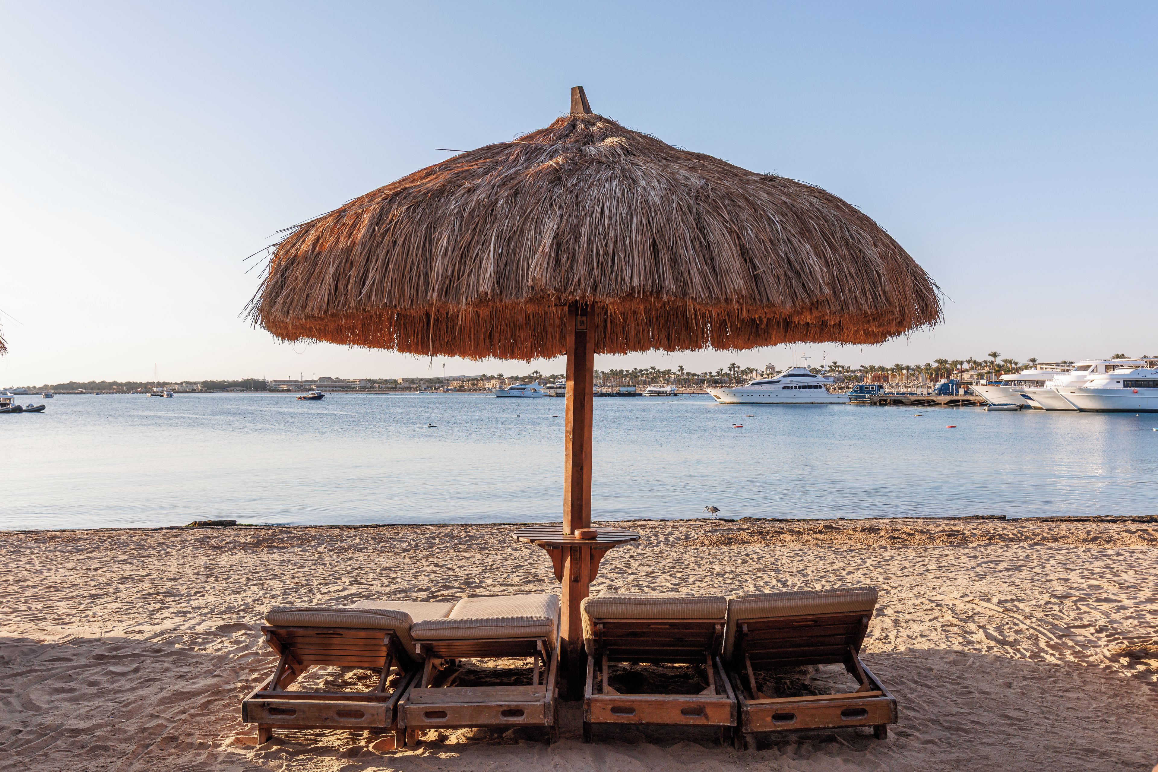Una playa con una sombrilla de paja y sillones de madera.