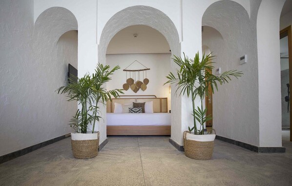 Un'accogliente hall d'albergo con un letto centrale, due piante in vaso e un lampadario decorativo.