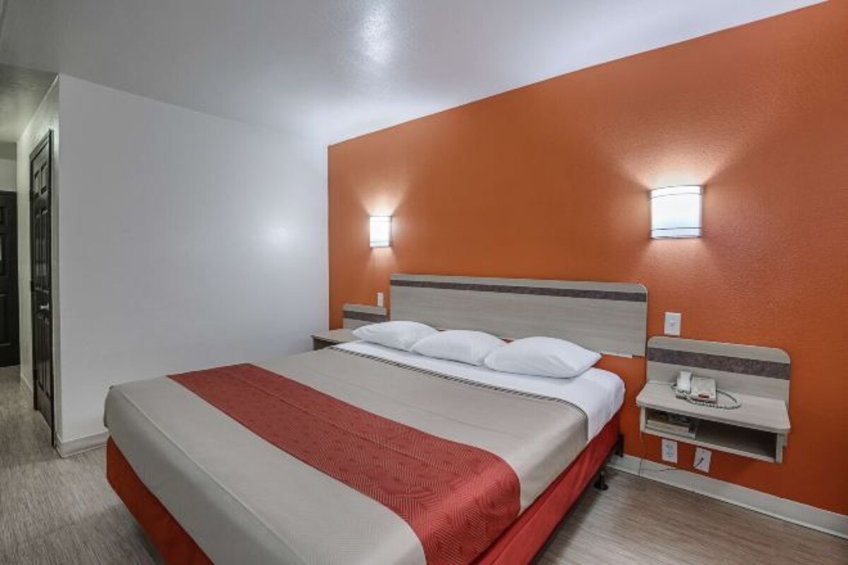 A hotel room with a bed, a nightstand, and a wall-mounted light fixture.