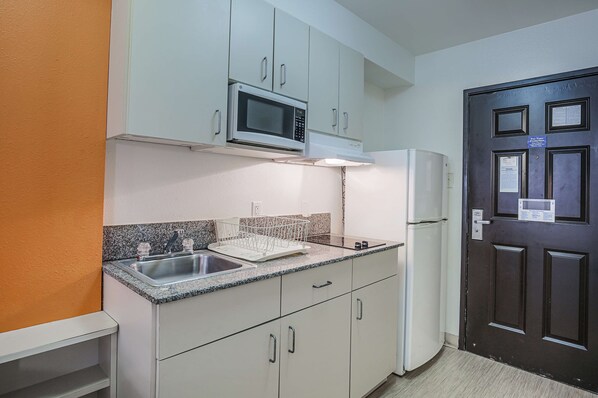 Una cocina compacta con armarios blancos, microondas, pileta con escurreplatos y refrigerador.