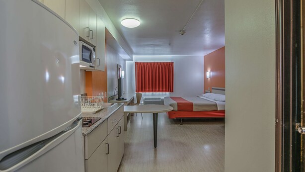 A compact hotel room with a kitchenette, a bed with red bedding, and a small table. - Motel 6 Pasadena, TX (Pasadena)