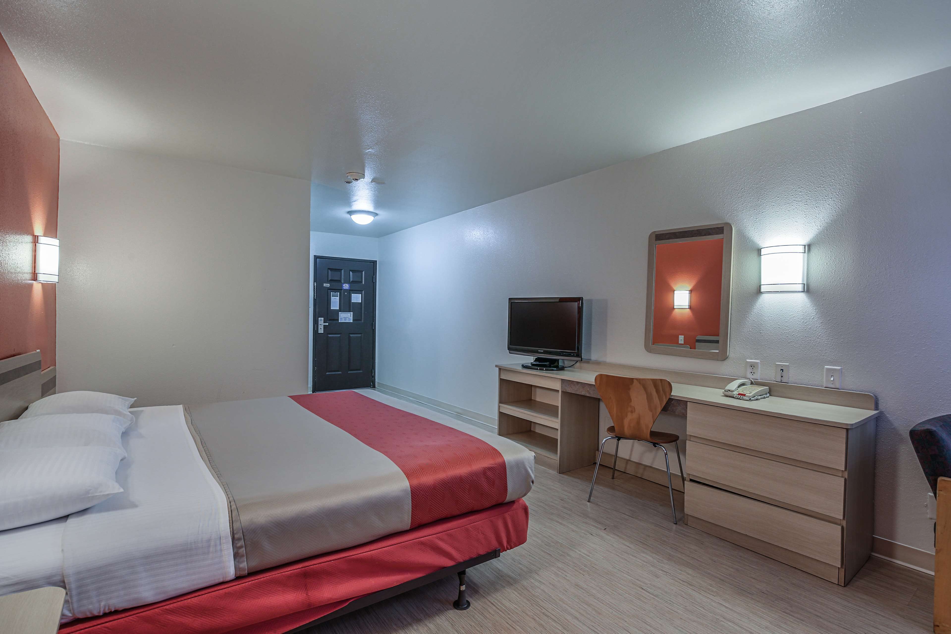 A hotel room with a bed, desk, chair, TV, and a door.