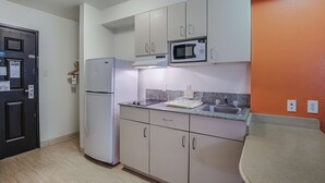 A compact kitchen with white cabinets, a microwave, a refrigerator, and a granite countertop. - Motel 6 Pasadena, TX (Pasadena)