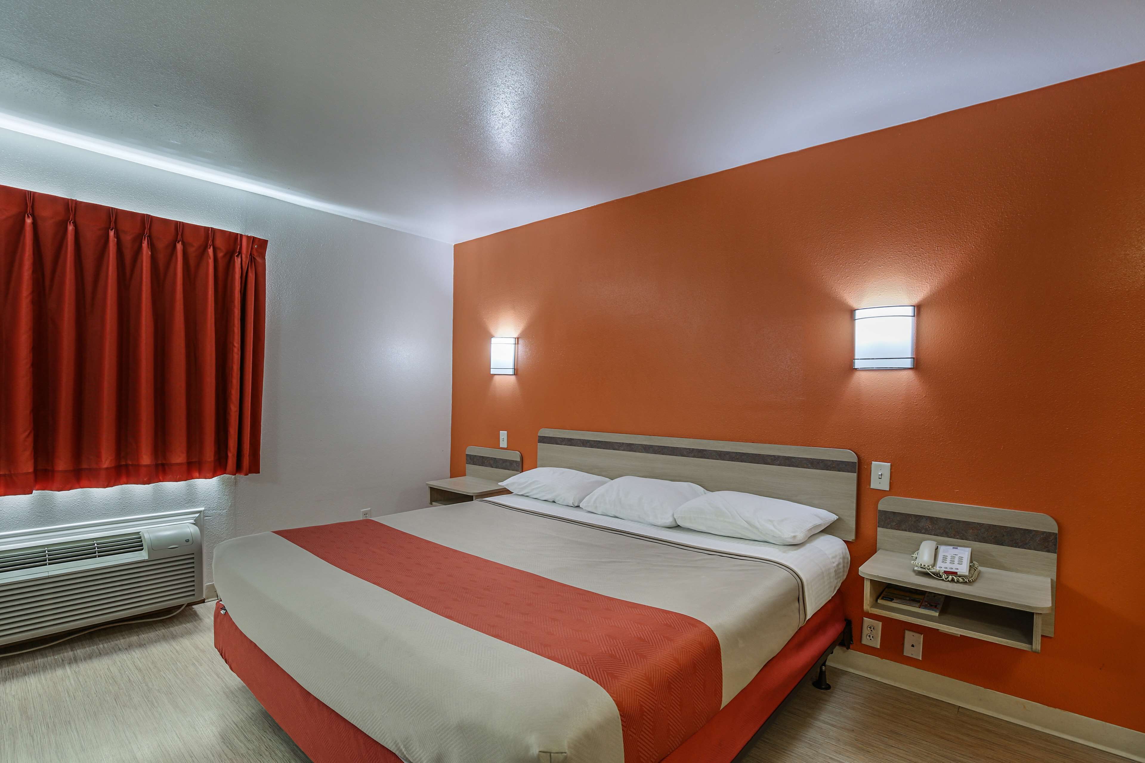 A hotel room with a bed, a nightstand, a telephone, and a wall-mounted light.