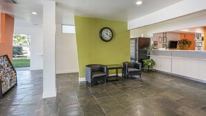 A reception area with a green wall, a clock, two leather chairs, a reception desk, and a magazine rack. - Motel 6 Pasadena, TX (Pasadena)