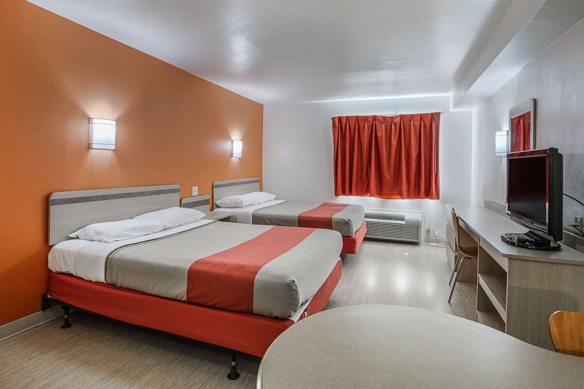 Quarto de hotel com duas camas, uma escrivaninha com televisão e banheiro com cortina.