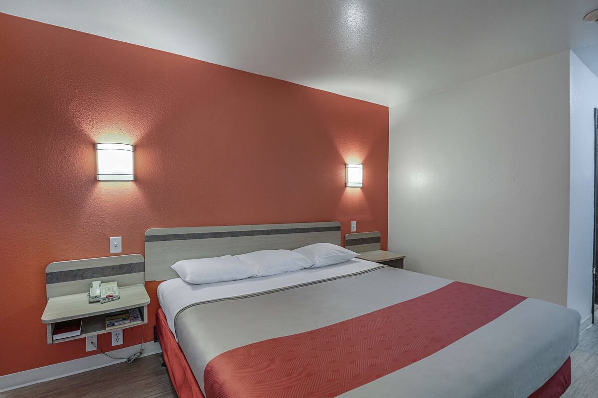 Quarto de hotel com uma cama, mesas de cabeceira e duas luminárias fixadas na parede.