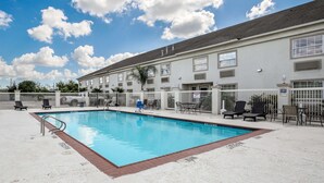 A swimming pool with lounge chairs and a fenced area, adjacent to a building with multiple windows and a flat roof. - Motel 6 Pasadena, TX (Pasadena)