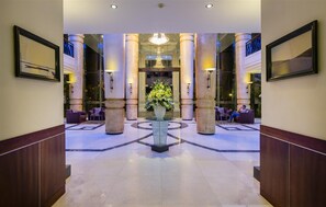 Un hall d’entrée spacieux agrémenté d’une composition florale centrale, de grandes colonnes et de coins salon.