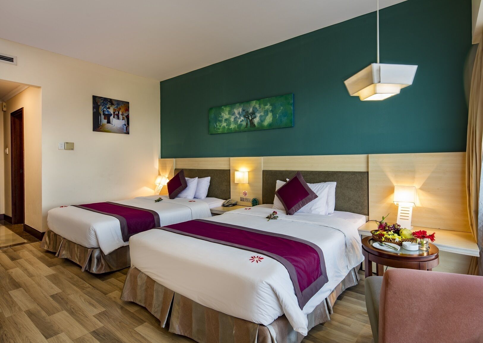 Een hotelkamer met twee bedden, een schilderij aan de muur en een tafel met fruit en bloemen.