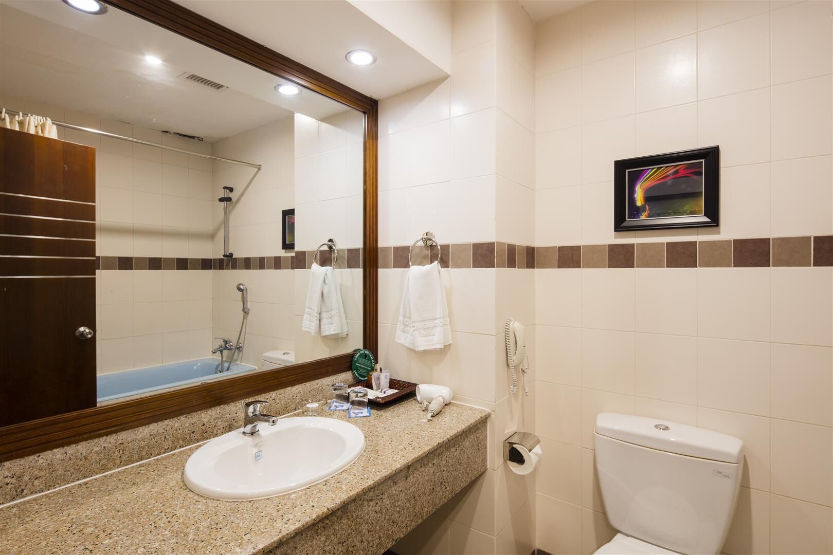 A bathroom with a sink, mirror, towel rack, shower, toilet, and a framed picture on the wall.