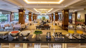 A spacious hotel dining area with multiple tables, a buffet counter with various food items, and a modern chandelier. - Sai Gon Quang Binh Hotel (Dong Hoi)