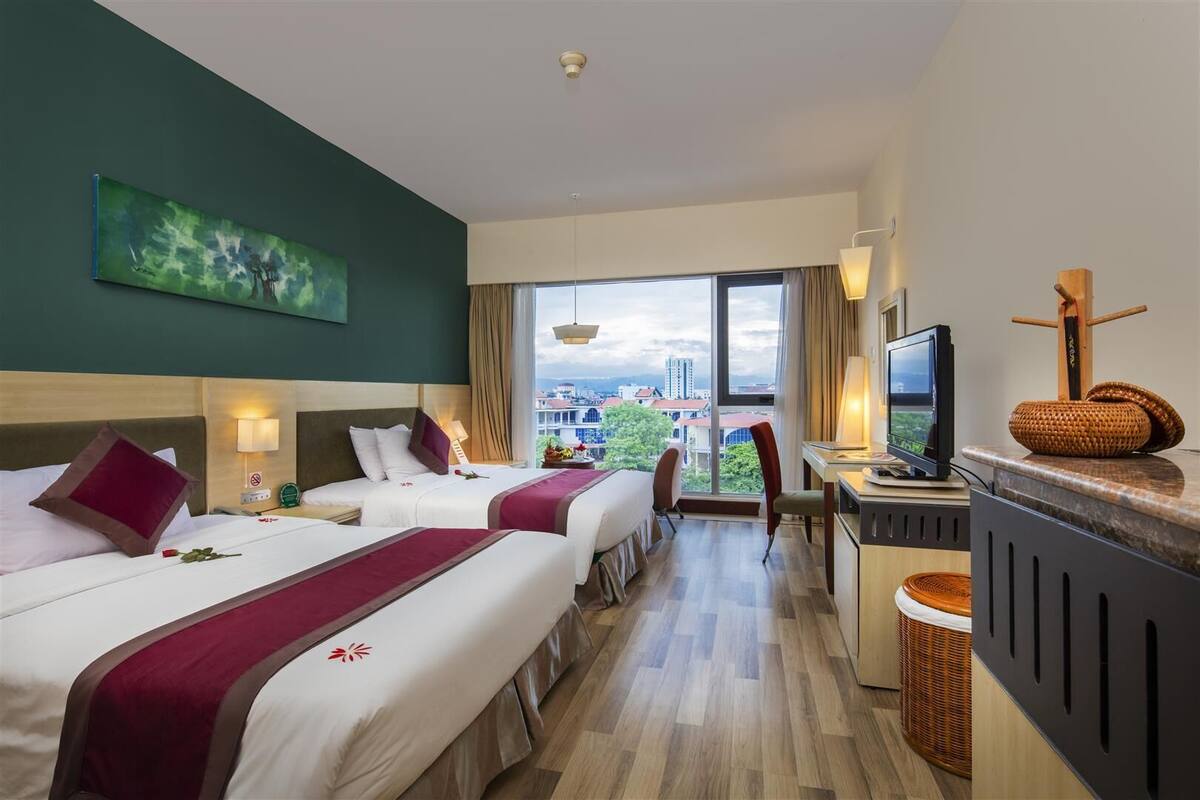 A hotel room with two beds, a desk, a TV, and a view of the city.