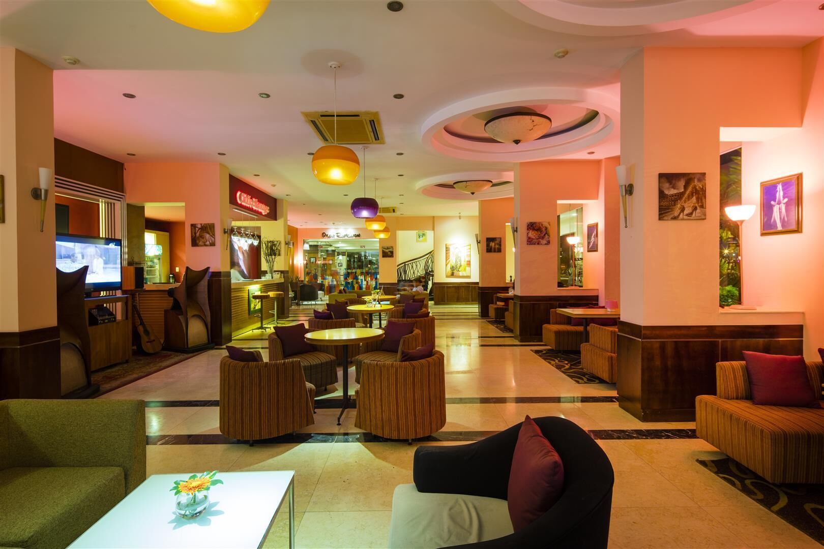 A hotel lobby with round tables, cushioned seating, a TV, and artwork on the walls.