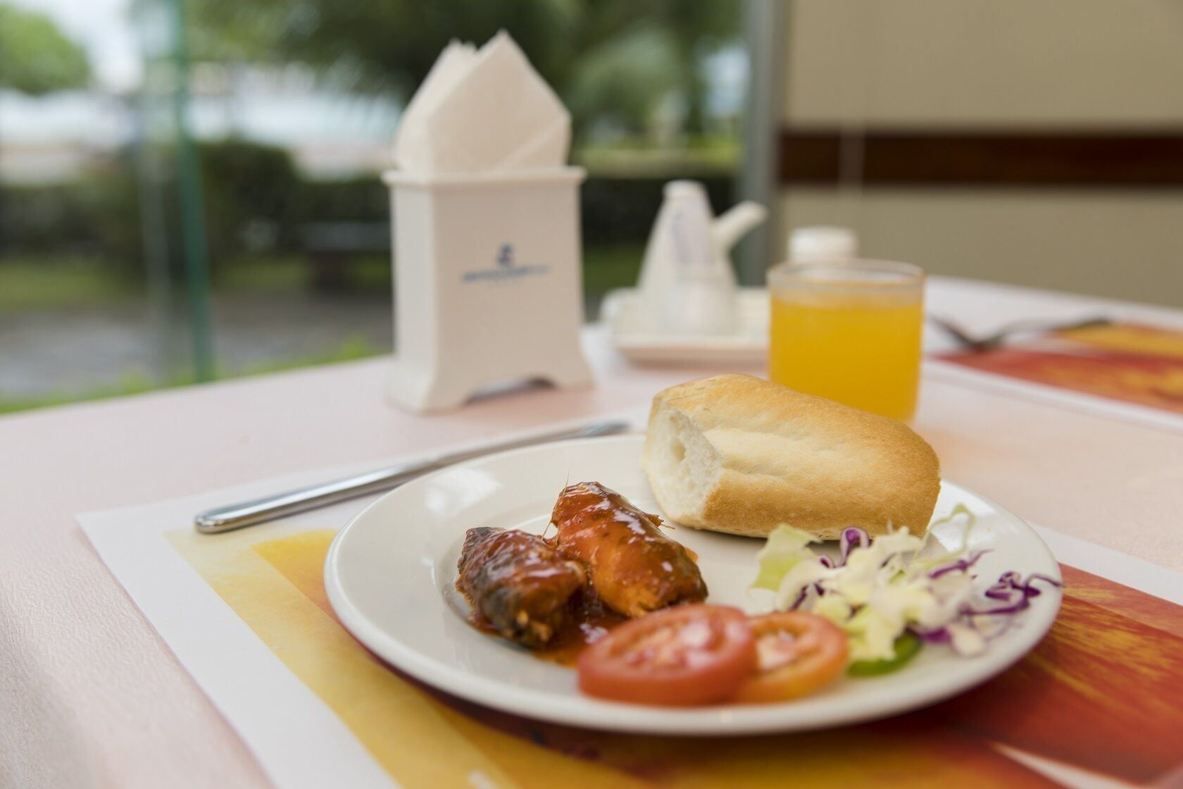 A plate with food, a napkin holder, a glass of orange juice, and a teapot on a table.