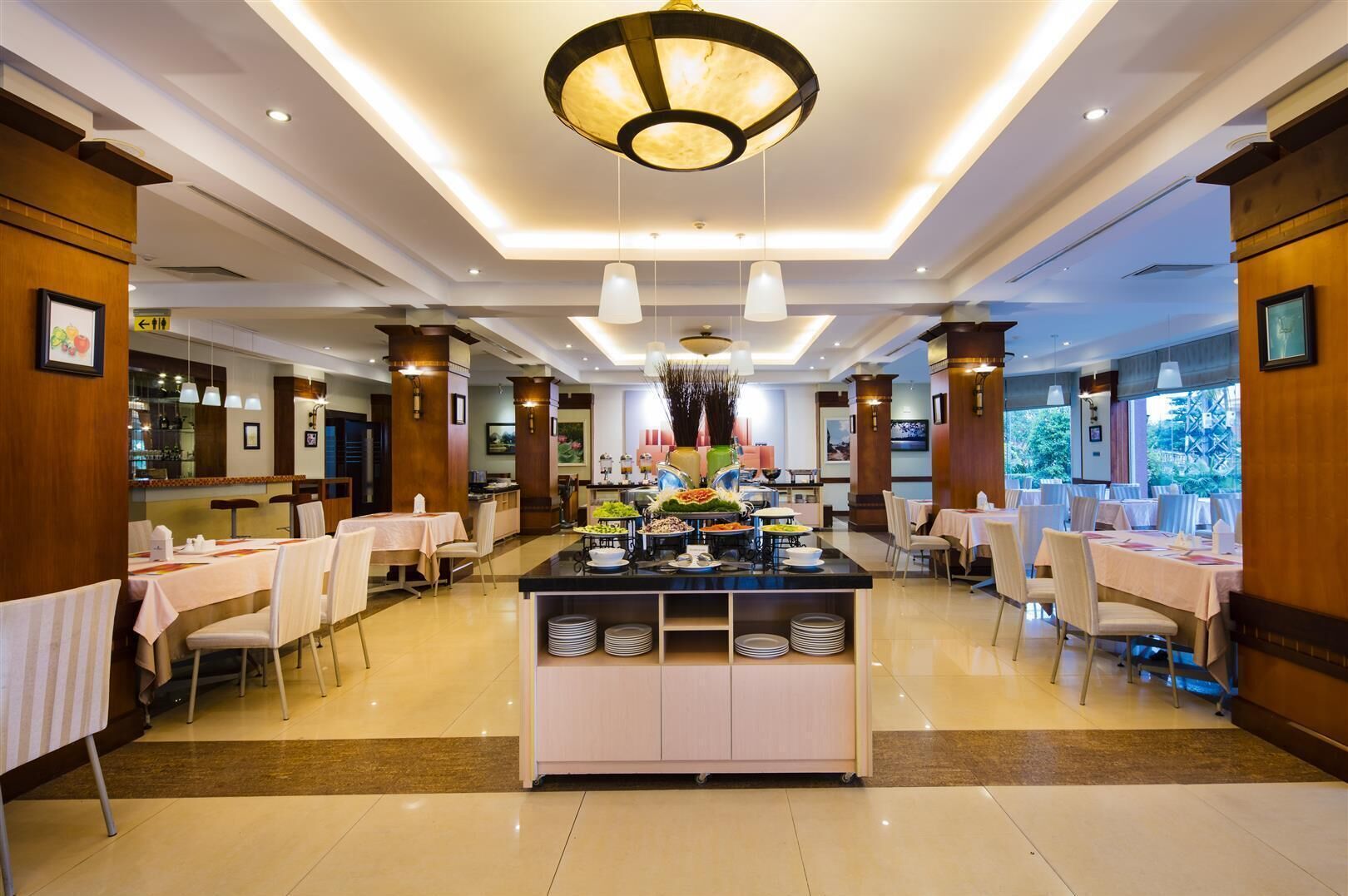 Un comedor de hotel con un bufé central, varias mesas y una araña.