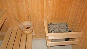 Ein Holz-Saunaraum mit einer Bank, einem Eimer und einem mit Steinen gefüllten Behälter.