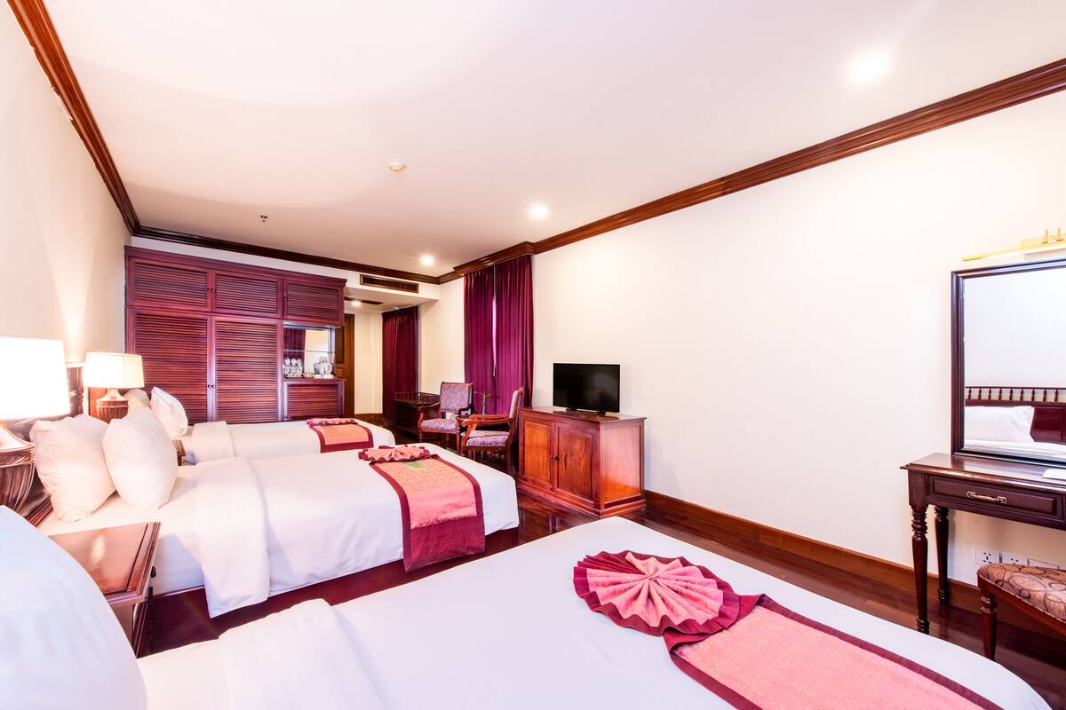 A hotel room with two beds, a television, a desk, and a mirror.