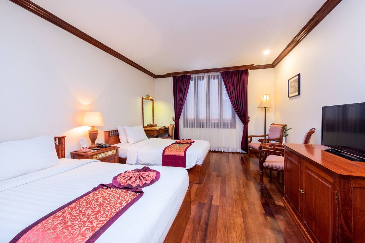 A hotel room with two beds, a desk, a TV, and a wooden floor.