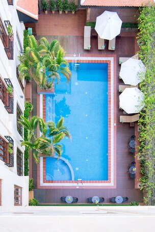 A rooftop pool with a blue mosaic border, surrounded by palm trees and outdoor seating.