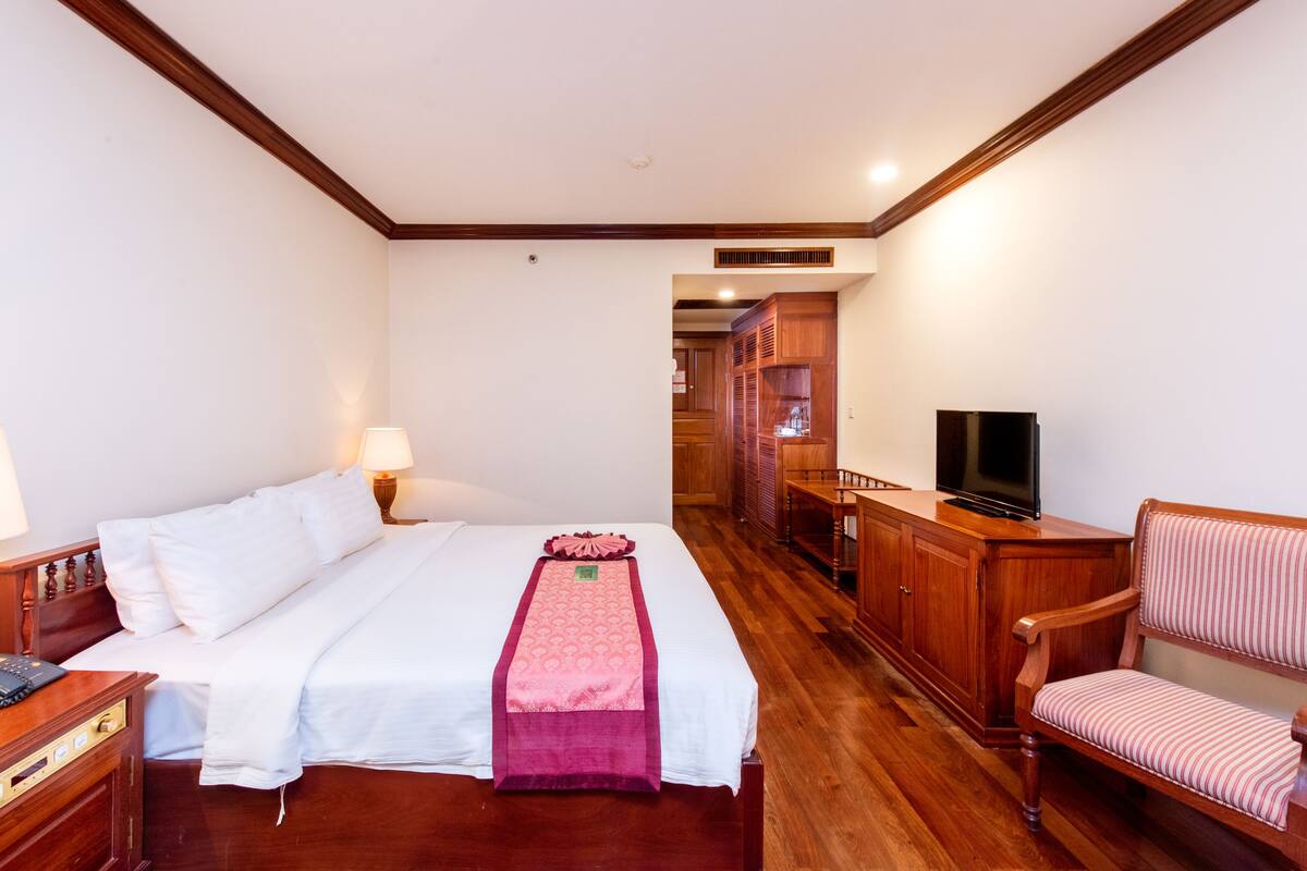 A hotel room with a bed, a TV, a wooden cabinet, and a chair.