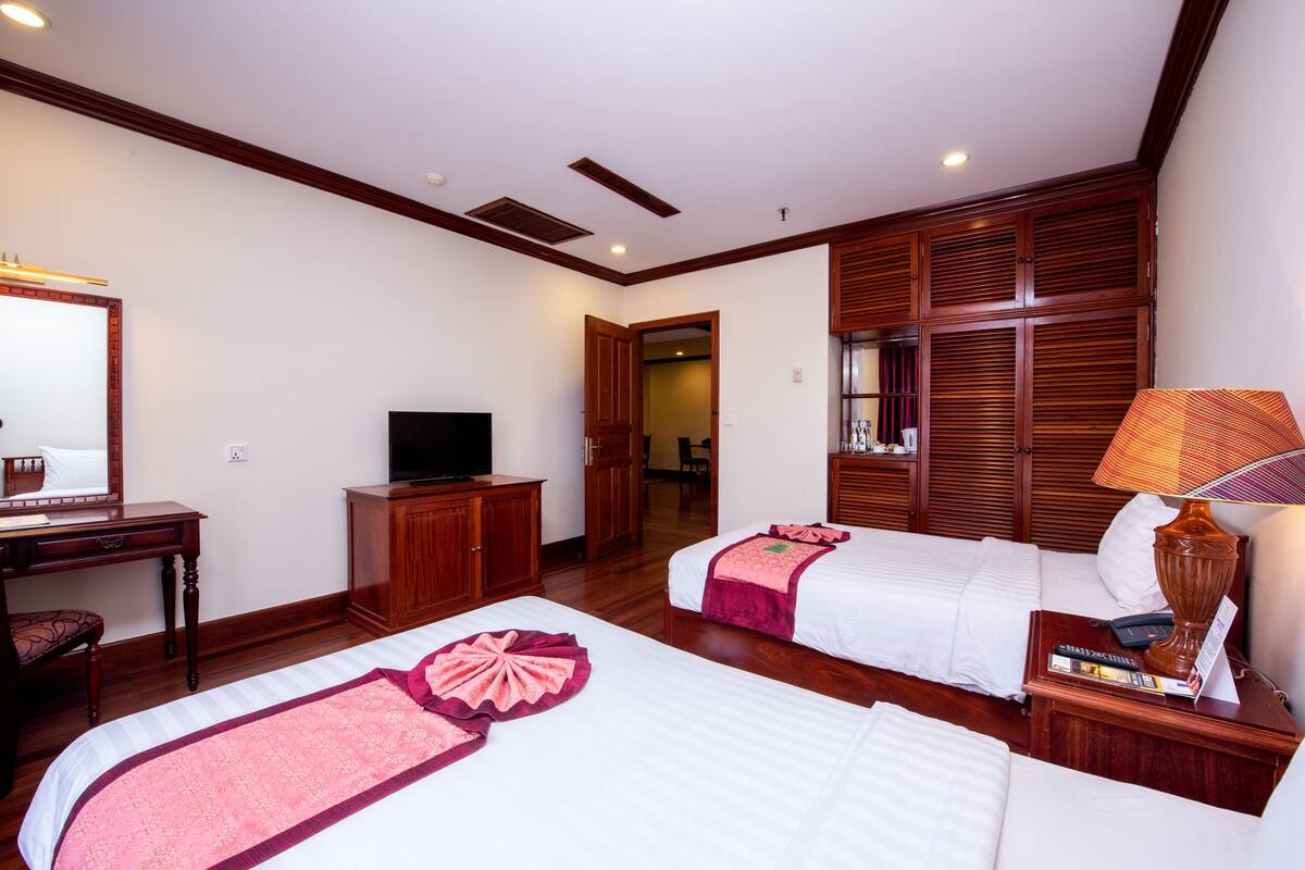 A hotel room with two beds, a desk with a TV, a lamp, and a wardrobe.