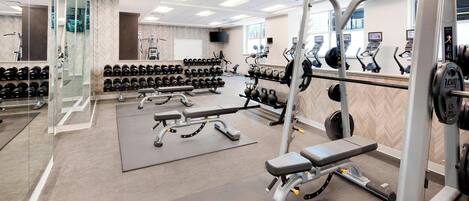 Un gimnasio con equipo de levantamiento de pesas, cintas de correr y un espejo grande.