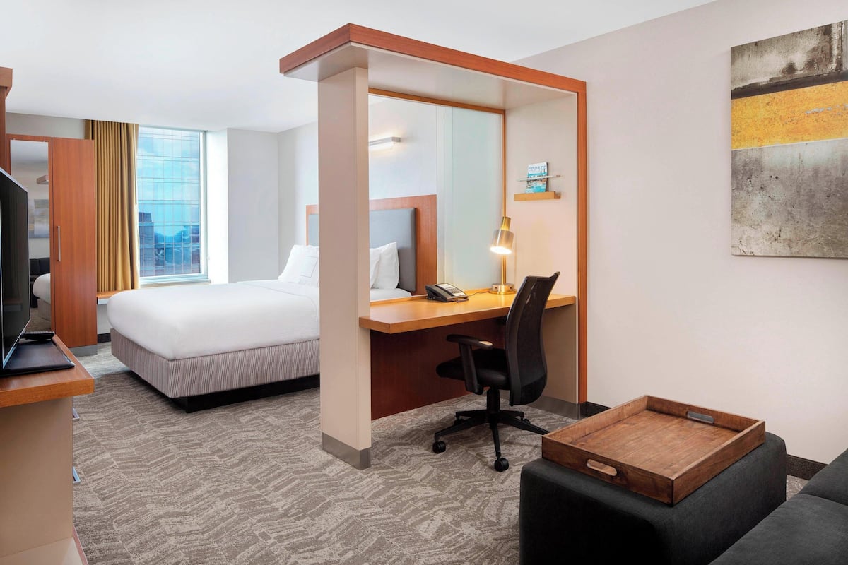 Une chambre d’hôtel avec un lit, un bureau, une chaise et une petite table en bois.