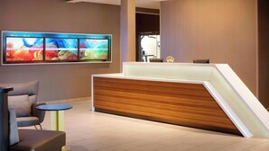 A reception area with a modern reception desk, a seating area with a chair and a small table, and a large abstract painting on the wall. - SpringHill Suites by Marriott Indianapolis Downtown (Indianapolis)