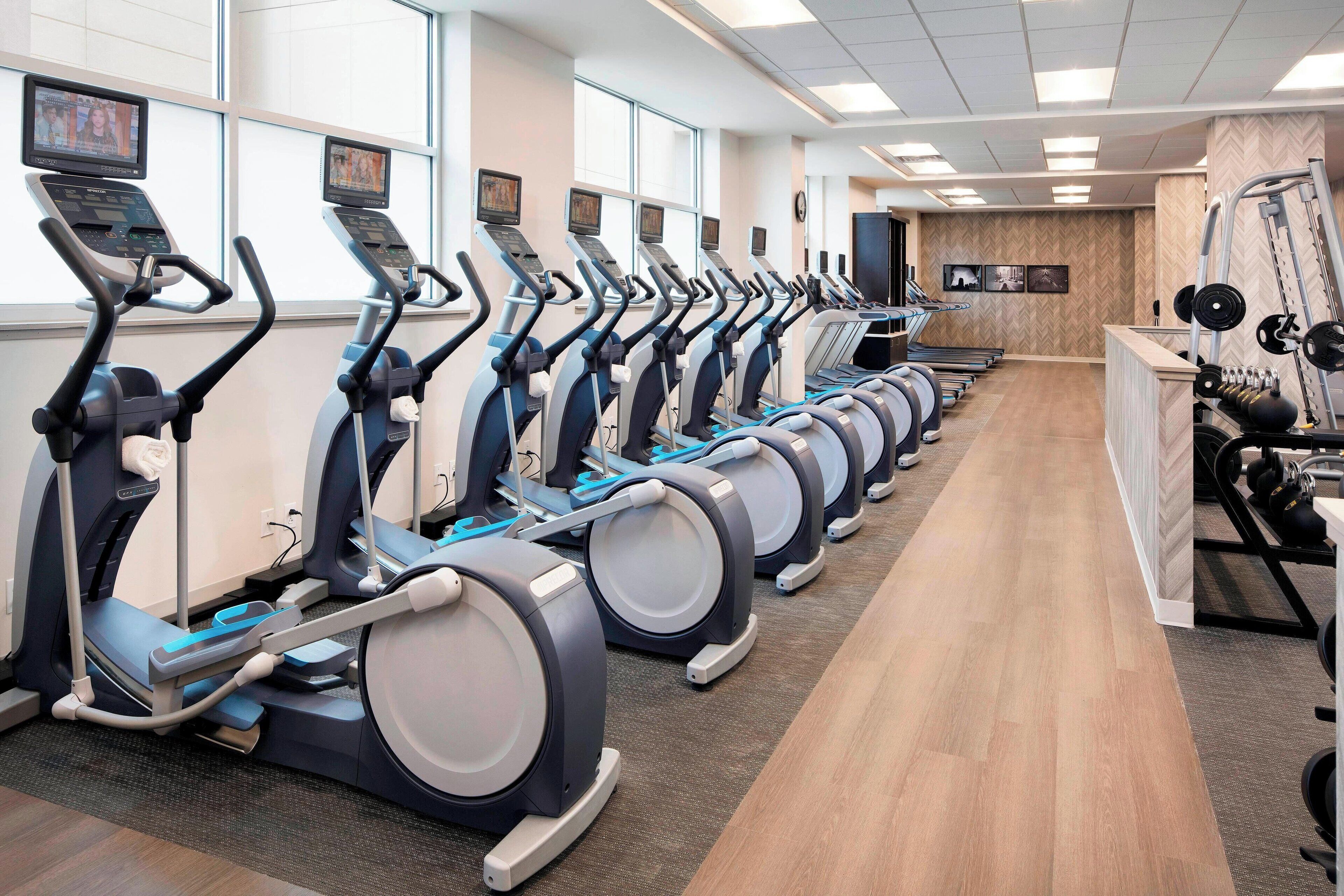 Varias bicicletas estáticas en un gimnasio con piso de madera y una televisión instalada en la pared.