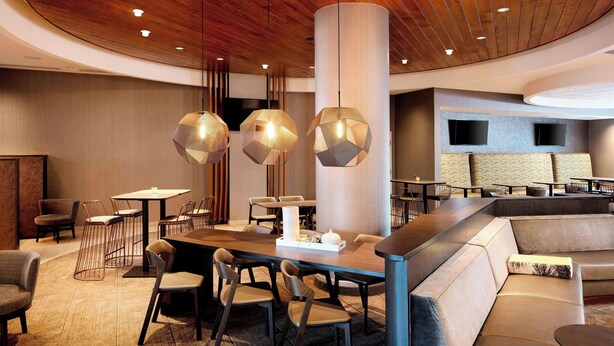 A modern hotel lobby with a curved wooden ceiling, a central seating area with sofas and chairs, and pendant lighting. - SpringHill Suites by Marriott Indianapolis Downtown (Indianapolis)