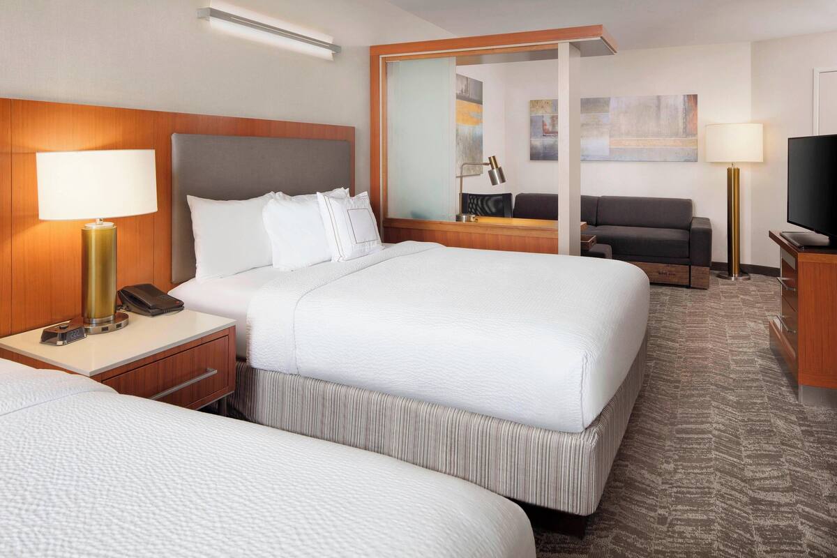 Une chambre d’hôtel avec deux lits, un bureau avec une lampe, une télévision et un canapé.