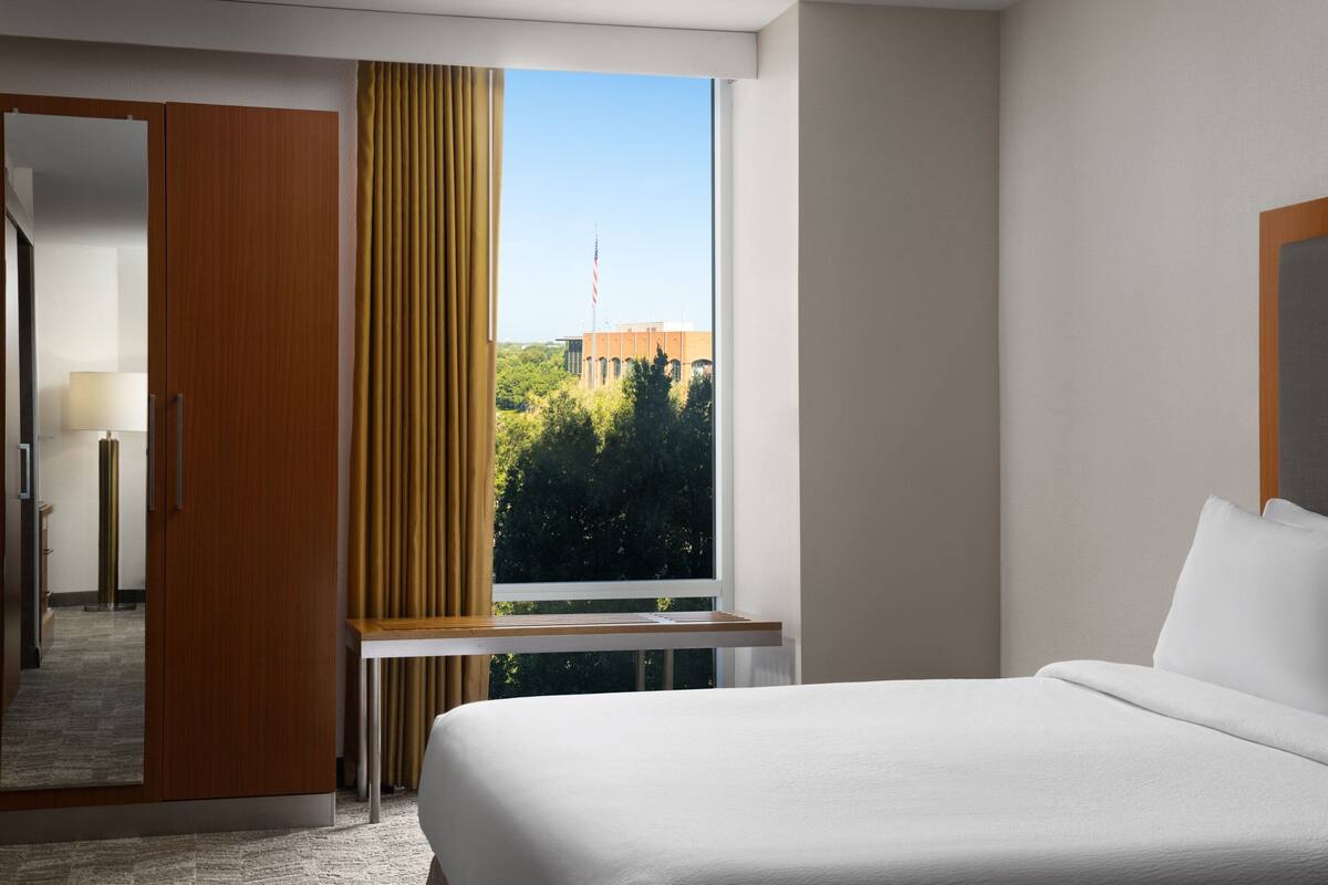 Une chambre d’hôtel avec une grande fenêtre, un lit, une armoire et un miroir.