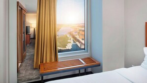 A hotel room with a large window, a bed, a wooden bench, and a view of a cityscape. - SpringHill Suites by Marriott Indianapolis Downtown (Indianapolis)