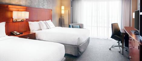 A hotel room with two beds, a desk, a chair, a lamp, and a television.