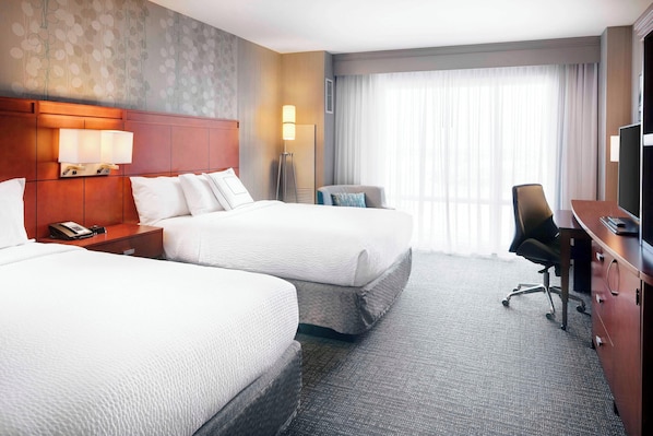 A hotel room with two beds, a desk, a chair, a lamp, and a television. - Courtyard by Marriott Indianapolis Downtown (Indianapolis)