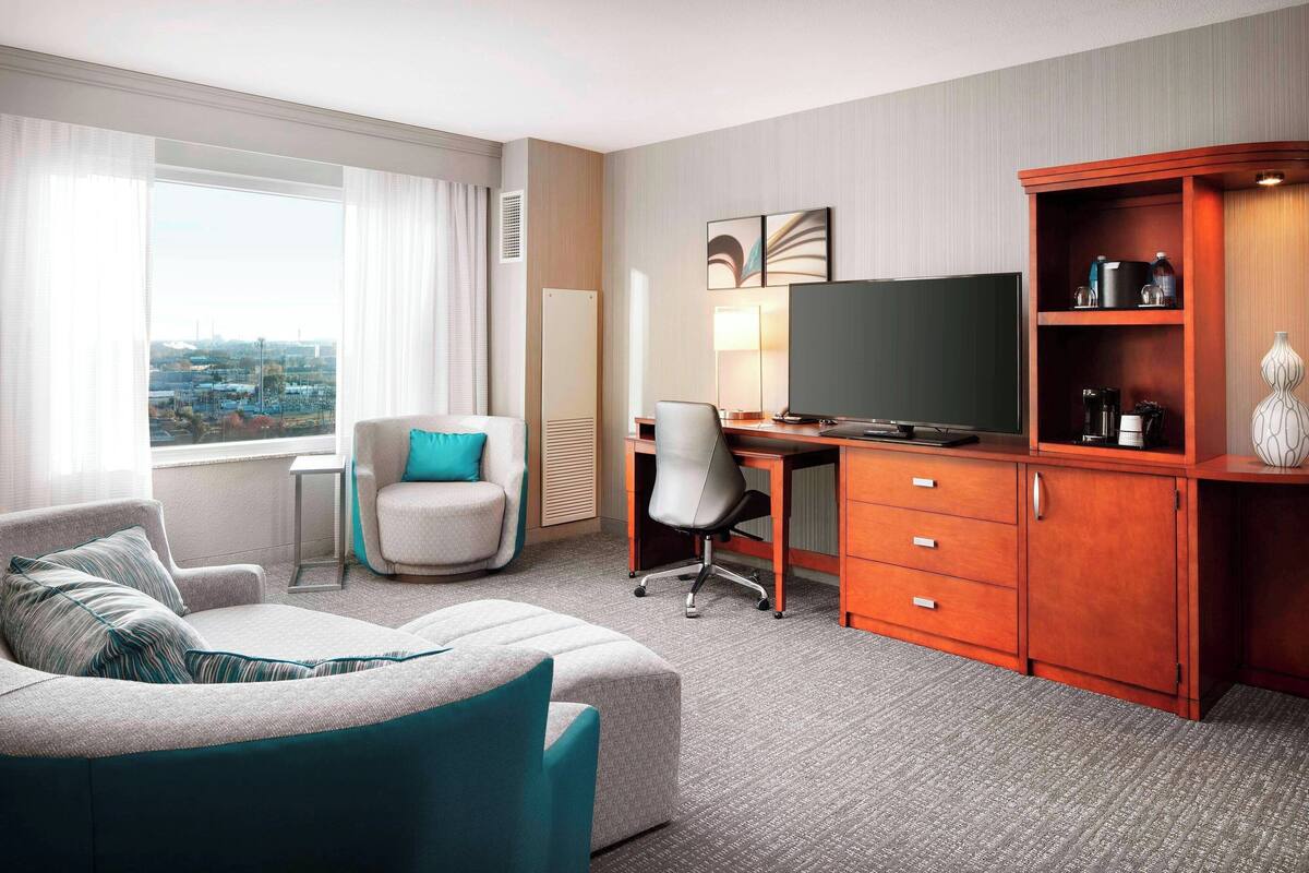 A hotel room with a sofa, a desk, a television, and a cabinet.